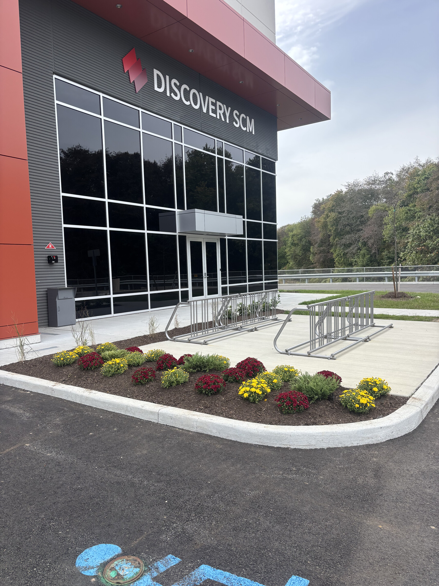 Commercial warehouse entrance with seasonal mum bed and freshly mulched landscape beds at a Discovery SCM logistics property in Mercer County, NJ. New Dawn Landscaping.